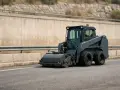 Macchina operatrice compatta, grigia, con rullo frontale, si muove su strada asfaltata. Le macchine operatrici, anche a bassa velocità, sono essenziali per lavori stradali.