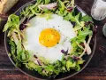 Un uovo occhio di bue su un letto di insalata mista, servito con pane integrale e condimenti.