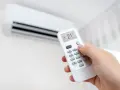 Mano ajustando el aire acondicionado a 21°C en modo "Cooling". La pantalla del control remoto muestra la temperatura y el modo, indicando que significa "cool" en el aire acondicionado: enfriar.