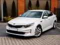 Biała Kia Ceed 1.6 benzyna zaparkowana na kostce brukowej, z ceglanym murem i tujami w tle.