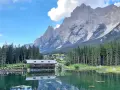 Riflessi alpini sul lago di Mosigo, con un rifugio e montagne imponenti sullo sfondo.