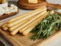 Grissini fatti in casa dorati e croccanti, profumati al rosmarino, pronti per essere gustati con formaggio e olive.