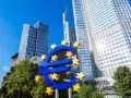 Symbol euro przed nowoczesnymi wieżowcami, siedziba europejskiego banku centralnego.