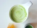 Zielony, spieniony napój matcha w białej miseczce, obok bambusowa miotełka i puszka z proszkiem. Idealne co na pobudzenie zamiast kawy.