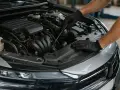 Meccanico con guanti neri lavora sul motore di un'auto, forse per la rigenerazione auto diesel.