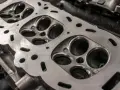 Nahaufnahme eines Zylinderkopfs eines Autos. Die Ventilsitze und die Bohrungen für die Zündkerzen sind sichtbar. Eine neue Kopfdichtung für das Auto wird bald montiert.