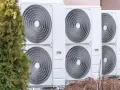 Unità esterne di climatizzatori, parte di un sistema di riscaldamento elettrico, allineate accanto a un albero verde.