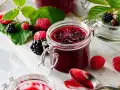 Frische Brombeeren und Himbeeren neben einem Glas selbstgemachter Marmelade. Perfekt für brombeeren rezepte schnell und einfach.