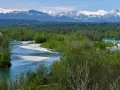 Il fiume Ticino serpeggia tra boschi rigogliosi, con montagne innevate all'orizzonte.