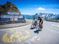 Ciclisti in salita verso il Col du Galibier, con montagne innevate sullo sfondo e segnaletica stradale.