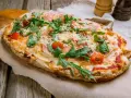 Pinsa co to? Aromatyczna, podłużna pizza z rukolą, pomidorkami i szynką parmeńską, posypana parmezanem.