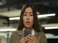 Młoda kobieta z zaskoczoną miną patrzy na ekran telefonu komórkowego.