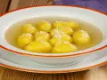 Una ciotola di semolino dosi per 1 persona, con palline dorate in brodo, cosparse di formaggio grattugiato.