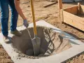Osoba kopie dół w betonie, przygotowując fundamenty pod słupki ogrodzeniowe. Właściwe proporcje betonu są kluczowe dla stabilności.