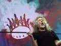 Wokalista Led Zeppelin, Robert Plant, śpiewa z pasją na tle scenografii z koroną.