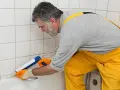 Mężczyzna w żółtym ogrodniczkach pokazuje, jak kłaść silikon w łazience, uszczelniając wannę.