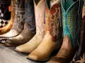 Una fila di stivali da cowboy colorati e ricamati, mostrando la differenza tra texani e camperos con vari design.