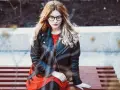 Dziewczyna w okularach i czerwonej sukience siedzi na ławce, ubrana w stylową kurtkę Dolce & Gabbana.