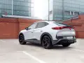 Biały elektryczny SUV Cupra Tavascan z czerwonymi akcentami na felgach, zaparkowany na tle ceglanego muru i nowoczesnych budynków.
