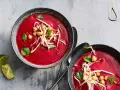 Zwei Schalen cremiger, **roter Bete Suppe mit Kokosmilch und Orangensaft**, garniert mit Kichererbsen und Sprossen.