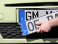 Dłoń trzyma nową tablicę rejestracyjną z literami "OE", gotową do zamontowania na samochodzie.