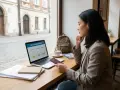 Kobieta analizuje opcje ubezpieczenia zdrowotnego na laptopie, trzymając paszport. W tle widać kawiarnię i ulicę.