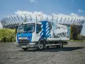 Ciężarówka szkoleniowa z literą "L" na masce, gotowa do nauki jazdy kat. C. W tle stadion.