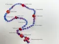 Ein Rosenkranz mit blauen und roten Perlen, beschriftet mit "Vater unser" und "Ave Maria". Die Rosenkranz Kette Bedeutung liegt in der Meditation und dem Gebet.
