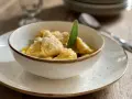 Gnocchi di zucca dorati e soffici, conditi con parmigiano e una foglia di salvia, serviti in una ciotola bianca su un piatto maculato.