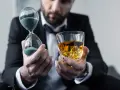Mann im Anzug hält Sanduhr und Whiskyglas. Die Frage, ob kann Whisky schlecht werden, wird durch die vergehende Zeit und den edlen Tropfen symbolisiert.