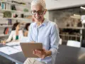 A smiling woman reviews a board chair job description on a tablet in a modern office.