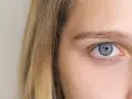Błękitne oko z jasną tęczówką, gdzie szpilkowate źrenice charakterystyczne są. Blond włosy opadają na twarz.