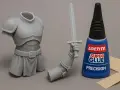 A grey resin knight model, its arm holding a sword, and a bottle of Loctite Super Glue Precision. Learn how to glue resin models for your next project.