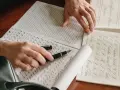 Manos practicando caligrafía con una pluma para colorear, practicando letras y formas en papel cuadriculado y con guías.
