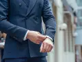 Uomo che sistema il polsino della sua giacca blu, un perfetto abbinamento giacca blu uomo per un look elegante.