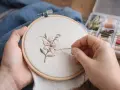Manos bordando una flor en un bastidor. Se aprecian hilos de colores y las medidas de los bastidores son importantes para este arte.