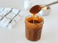 Une cuillère verse du caramel onctueux dans un pot. La recette caramel parfaite pour vos desserts.