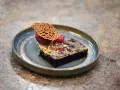 Elegancki deser: monoporcja brownie z malinami i lodami, ozdobiona listkiem z ciasta. Kontrastuje z tradycyjnymi blachami ciasta.