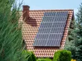 Nowoczesna instalacja fotowoltaiczna na dachu domu, otoczona zielenią.