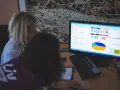 Dwie kobiety przy komputerze analizujące dane na ekranie, widoczny wykres i liczby.