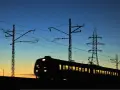 Pociąg w ruchu na tle zachodzącego słońca i linii energetycznych.