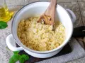 Ein Topf mit frisch gekochtem Couscous, bereit für ein einfaches Couscous-Rezept. Ein Holzlöffel rührt die Körner auf.