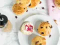 Goldbraune Scones mit Rosinen und Mandeln, ein Scones Teig mit Marmelade und Sahne, daneben ein Getränk.