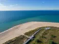 Piękne wydmy helskie nad turkusowym morzem. Drewniana kładka prowadzi przez zarośla na piaszczystą plażę, gdzie spacerują nieliczni turyści.