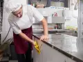 Cocinero con delantal limpiando encimera de acero inoxidable. Esencial para la limpieza de restaurantes.