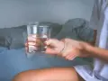Dłoń z drżącym szkłem wody, sugerującym zwidy po alkoholu. Rozmyte kontury i niepewny chwyt.