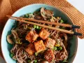 Pyszny makaron z tofu po azjatycku z grzybami i groszkiem, podany z pałeczkami.