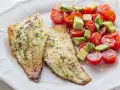 Dos filetes de lubina a la plancha con hierbas, acompañados de una ensalada fresca de tomates cherry y aguacate en cubos.