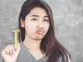 Mujer con expresión de disgusto sostiene una cuchilla amarilla, con pelos en la barbilla simulando bigote.