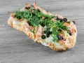 Pyszne ciasto na pizzę z szynką, mozzarellą, rukolą i czarnymi oliwkami na drewnianym tle.